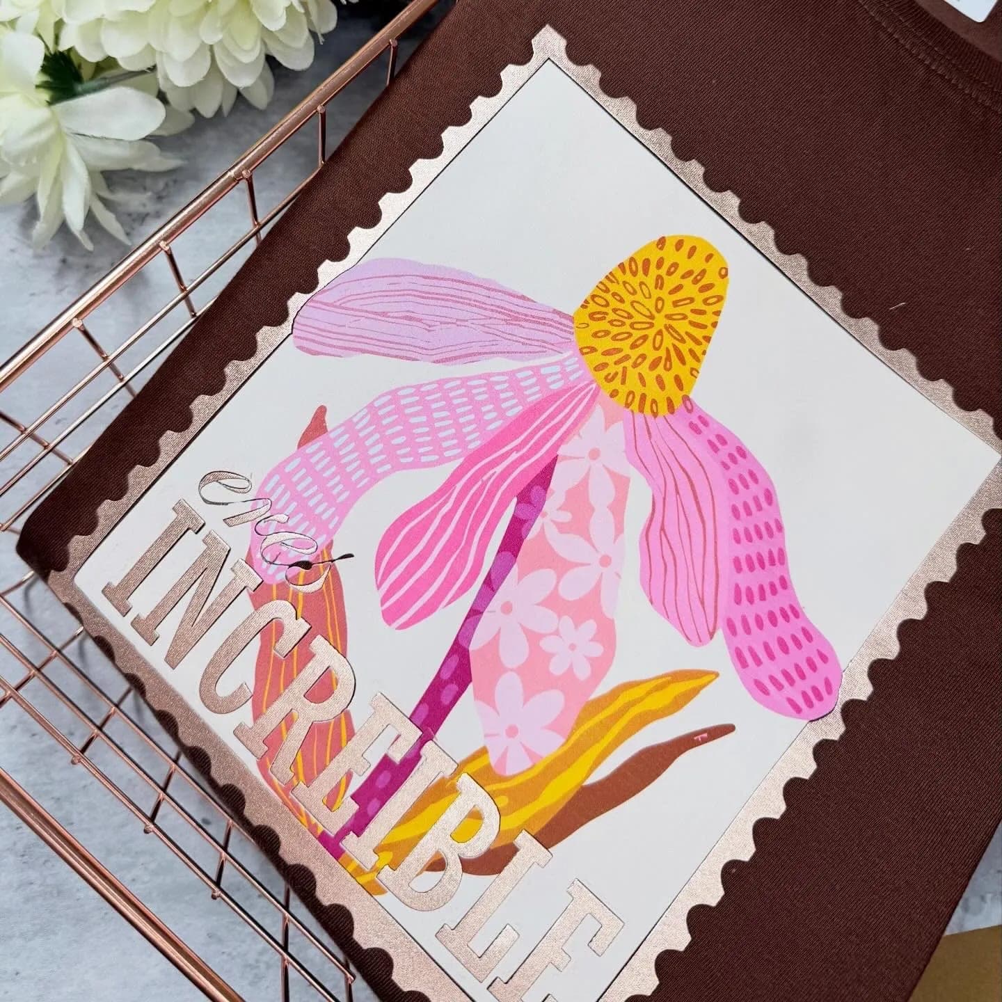 Camiseta chocolate con estampilla de flor y la frase Eres increíble en foil