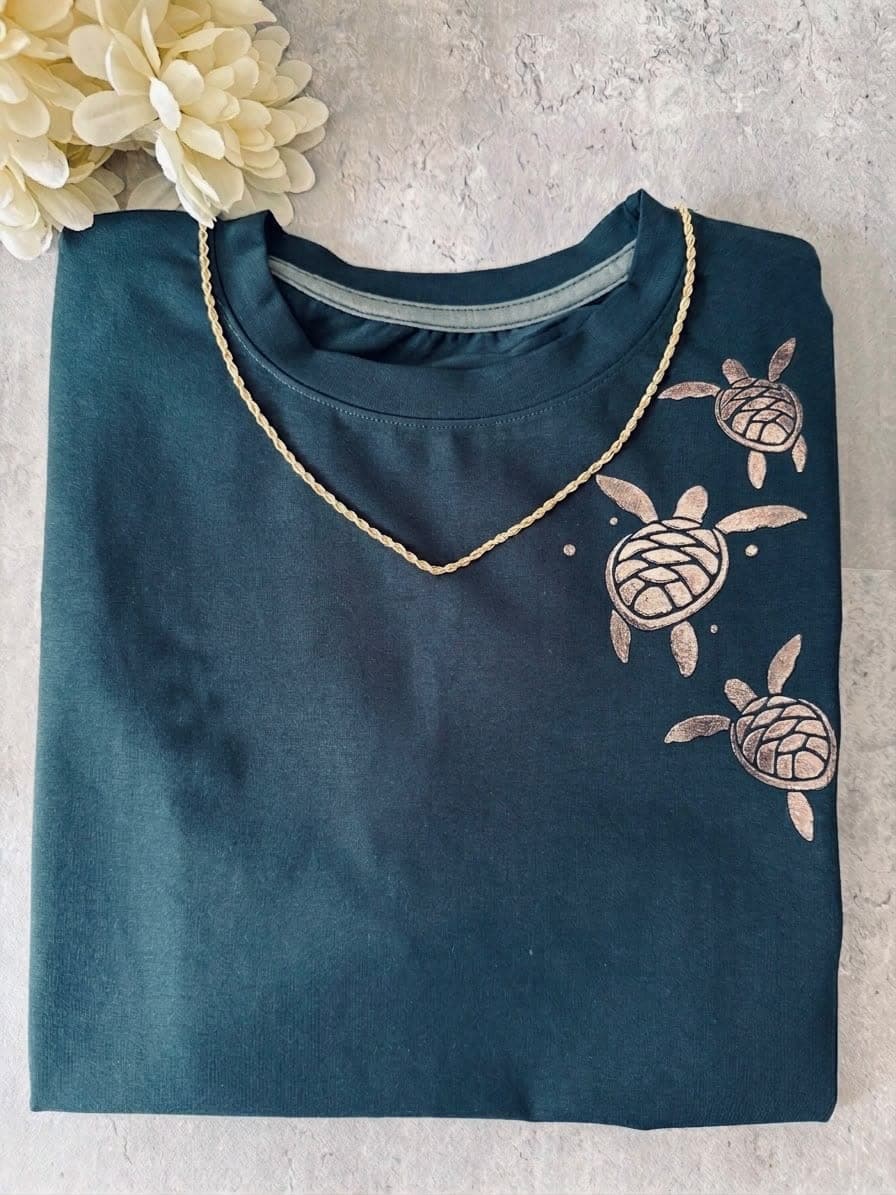 Camiseta verde pino con tres tortugas doradas cerca del hombro
