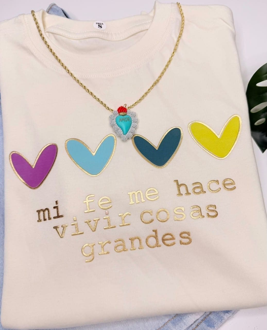 Camiseta crema en tela fría con corazones de colores y la frase Mi fe me hace vivir cosas grandes