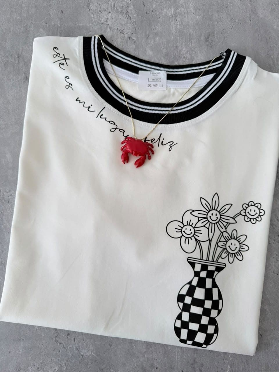 Camiseta blanca en tela fría con cuello negro, florero y la frase Este es mi lugar feliz