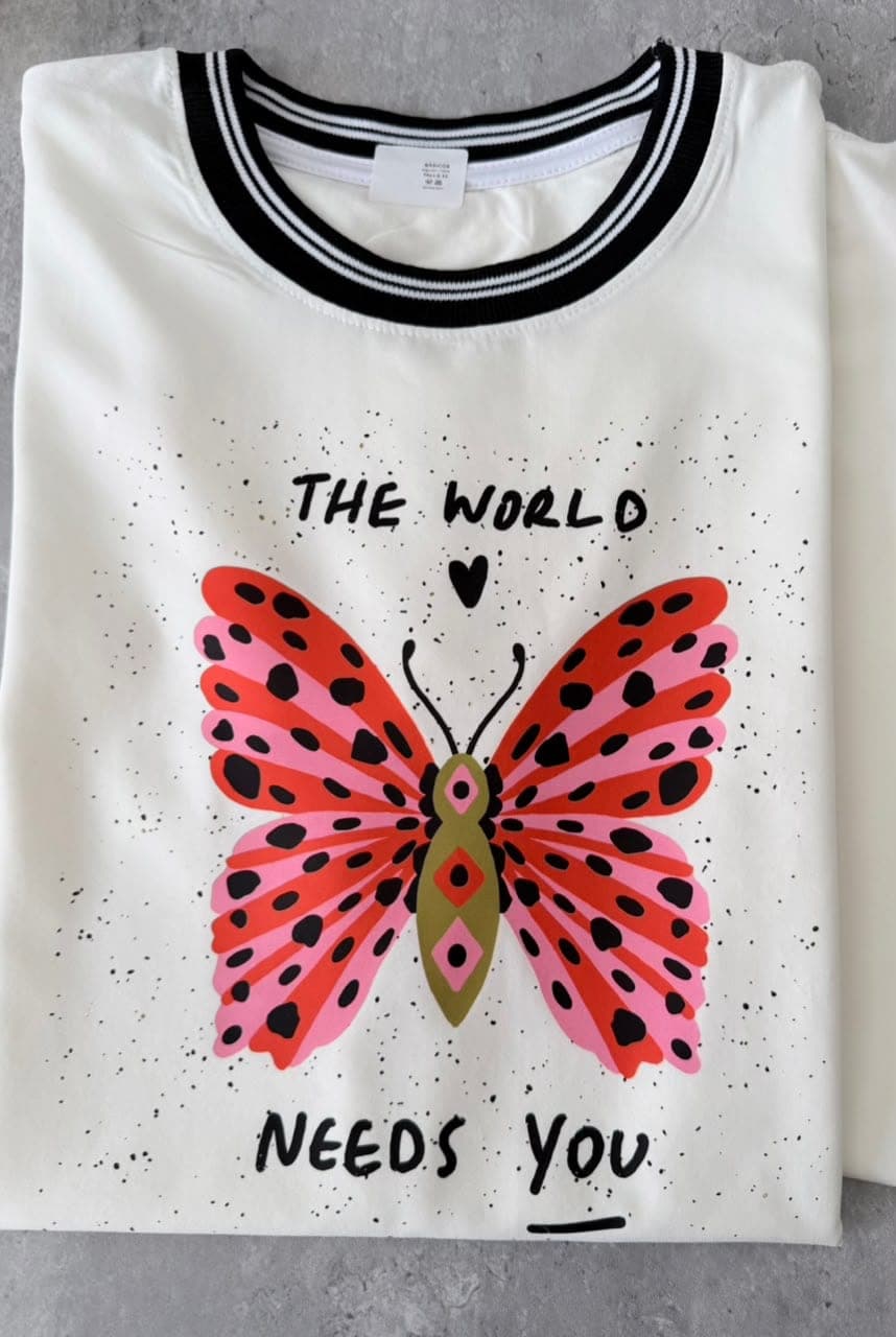 Camiseta crudo en tela fría con cuello negro, mariposa y la frase The world needs you